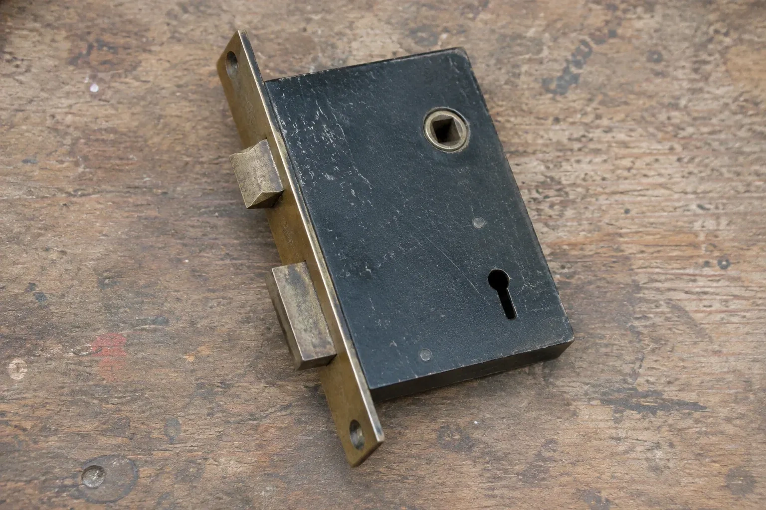 Closed mortise lock case with spindle opening, keyhole, latch and deadbolt on a wooden workbench. — Vintage Mortise Lock Service, Kawartha Lakes