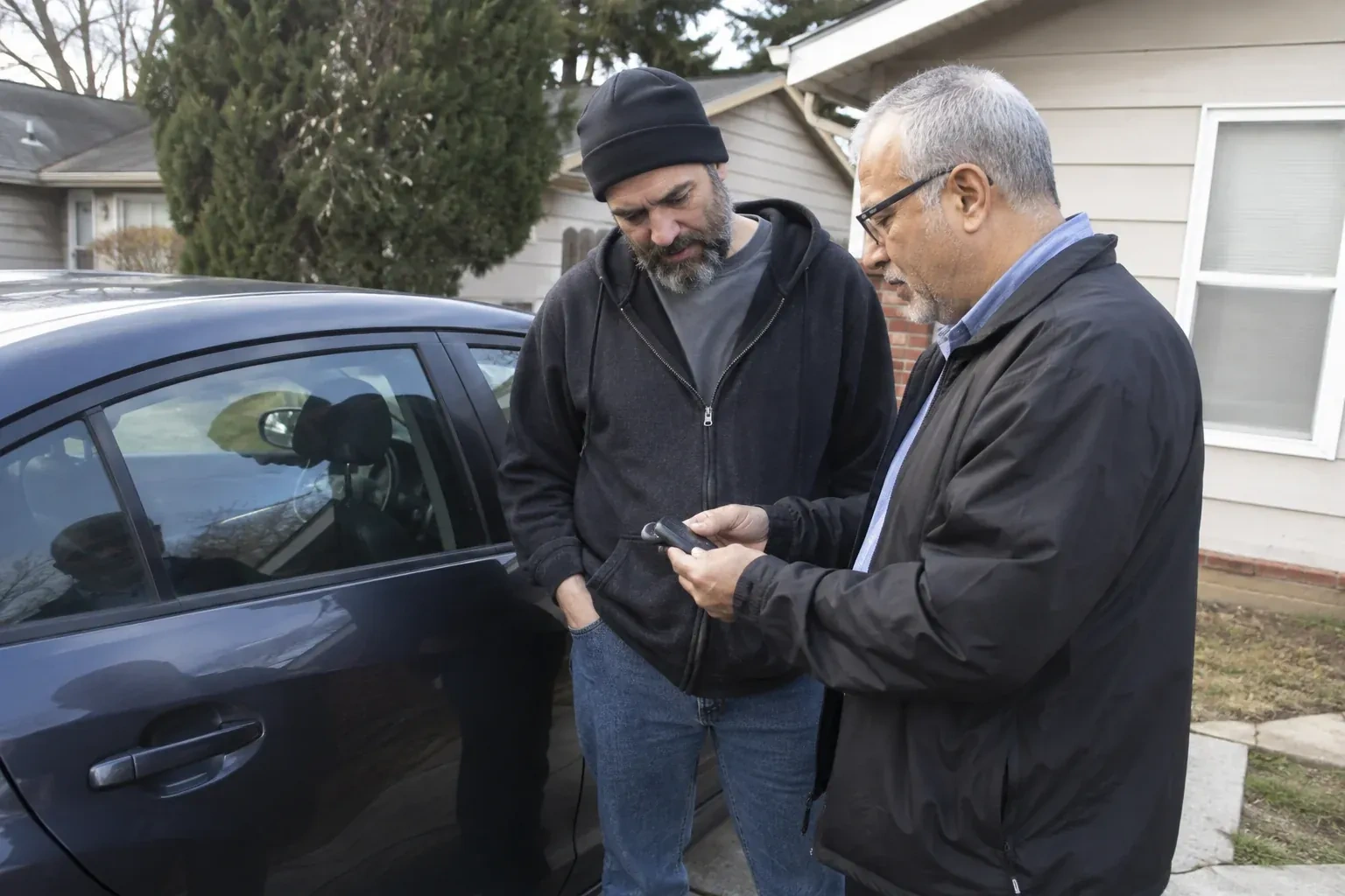 Two adults discussing a key fob beside a parked car. — Car Lockout Service, Kawartha Lakes